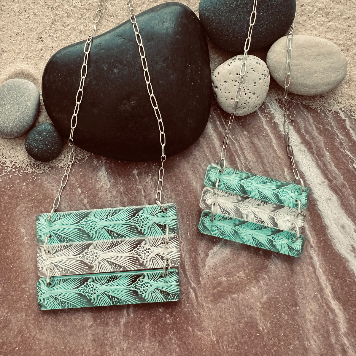 Sea Turtle Pattern 3 bar necklace in alternating green and white.  Shown in small and large size on a sandy rocky surface.