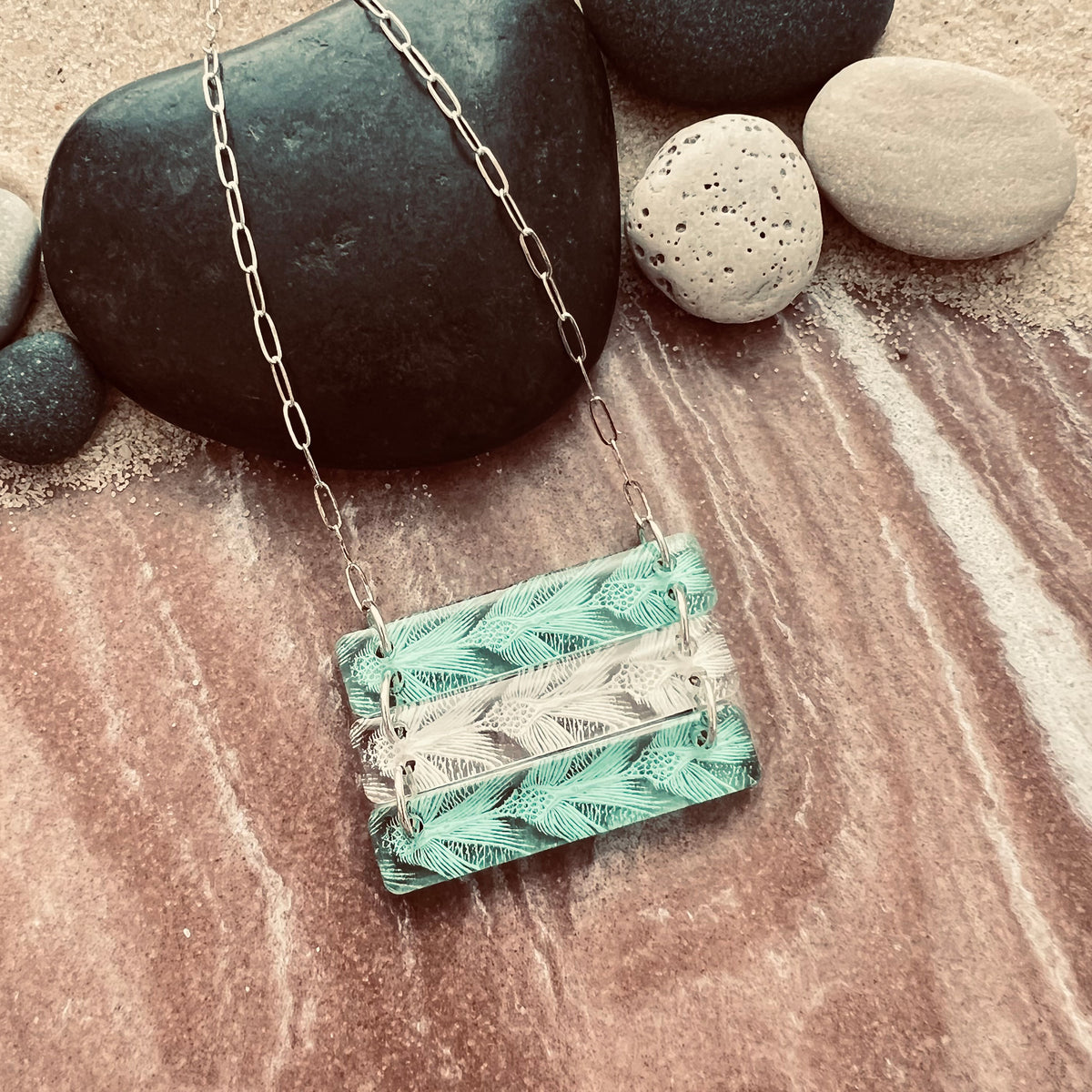 Sea Turtle Pattern 3 bar necklace in alternating green and white.  Shown in small size on a sandy rocky surface.