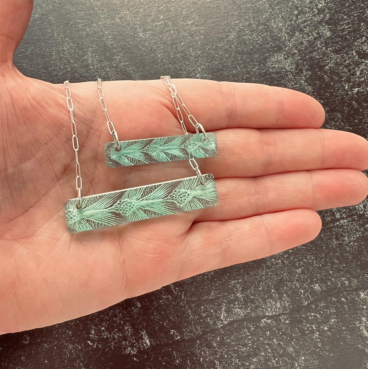 Size comparison of small and large bar Necklaces with sea turtle pattern in green in hand.