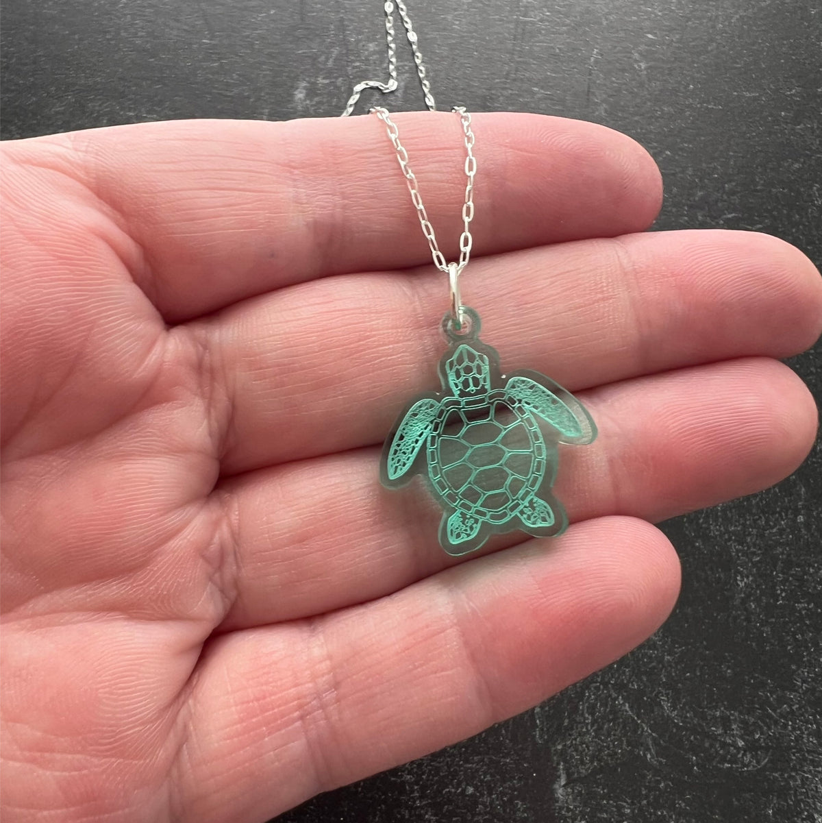 Sea turtle pendant on a sterling silver chain. Lightweight, Semi-transparent green laser cut acrylic. Lovely to wear to any occasion. Shown in hand to see size and transparent nature of the material